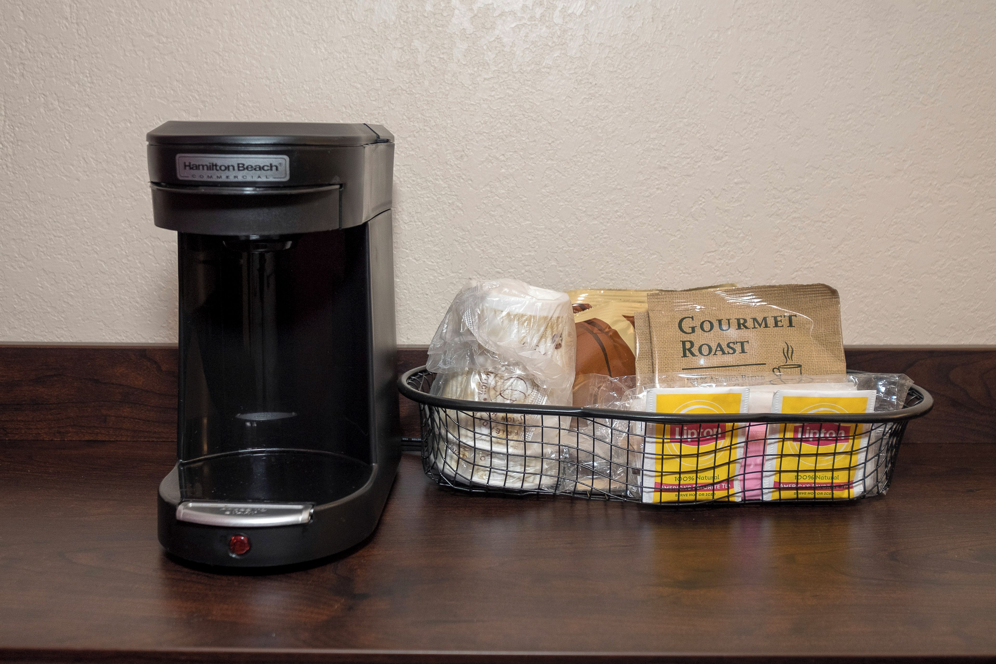 Una cafetera Hamilton Beach y una cesta con un paquete de café Gourmet Roast, bolsitas de té Lipton y otros artículos.