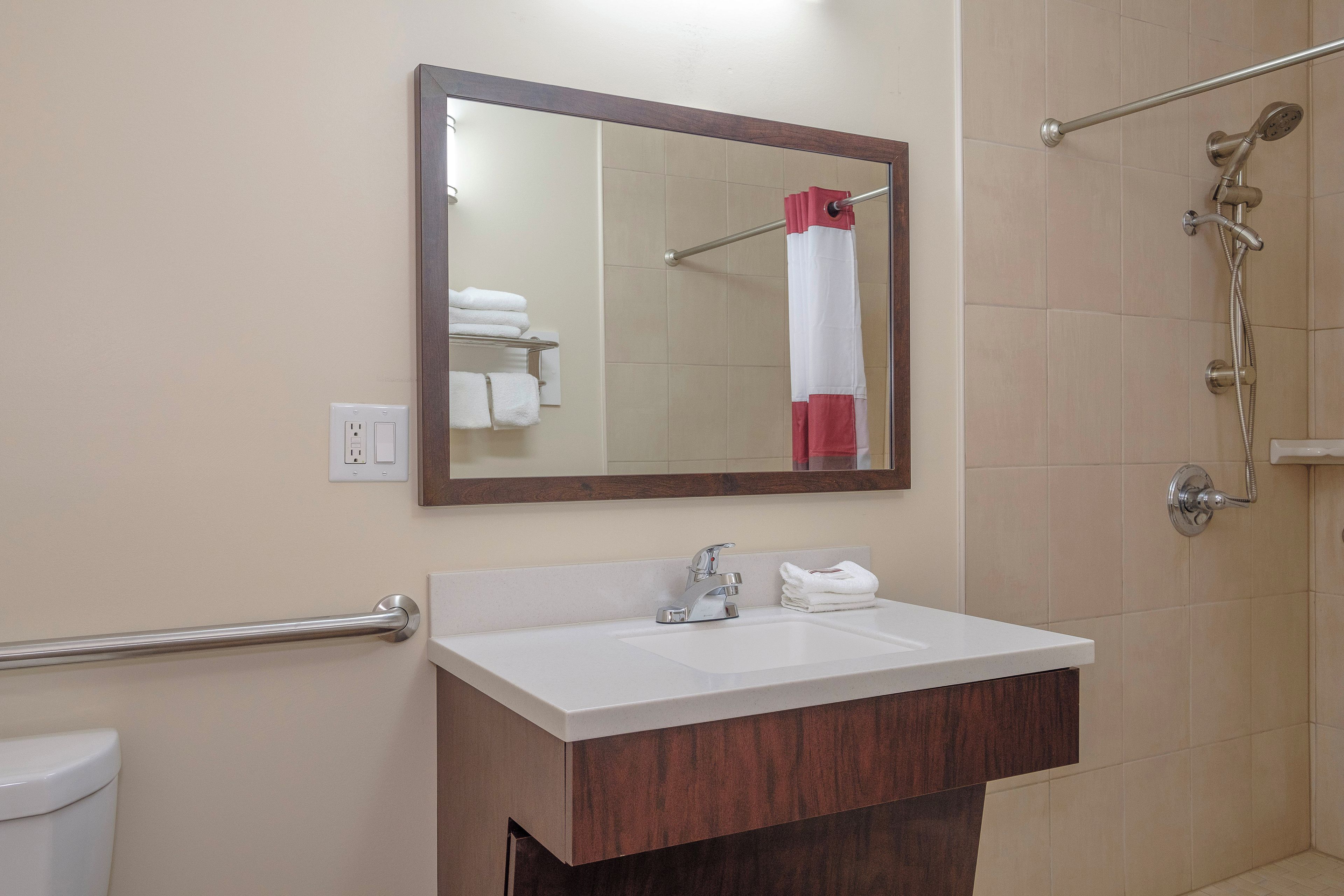 A bathroom with a white sink, a mirror, a towel rack, and a shower area.