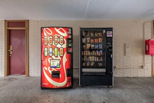 Dos máquinas expendedoras, una con el diseño de Coca-Cola y la otra con aperitivos, frente a un muro de ladrillo.