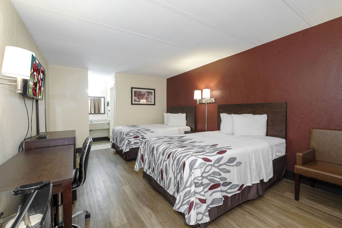 A hotel room with two beds, a desk, a chair, and a TV mounted on the wall.