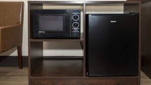 Una cocina compacta con microondas y un refrigerador negro sobre un mueble de madera.