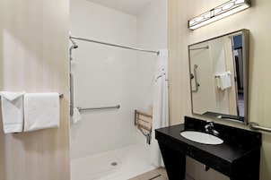 Un baño con ducha a nivel, lavamanos y espejo.