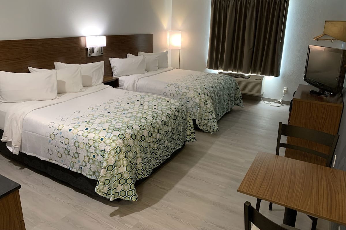 A hotel room with two beds, a desk, a chair, a television, and a window with curtains.