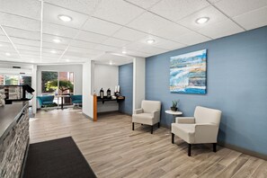 Eine moderne Lobby mit einer Rezeption, zwei Sitzbereichen mit Stühlen, einer Kaffeestation und einem großen Gemälde an der Wand.