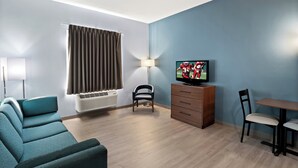 Un salon moderne avec un mur bleu, un canapé, un téléviseur, une lampe et une table à manger avec des chaises.