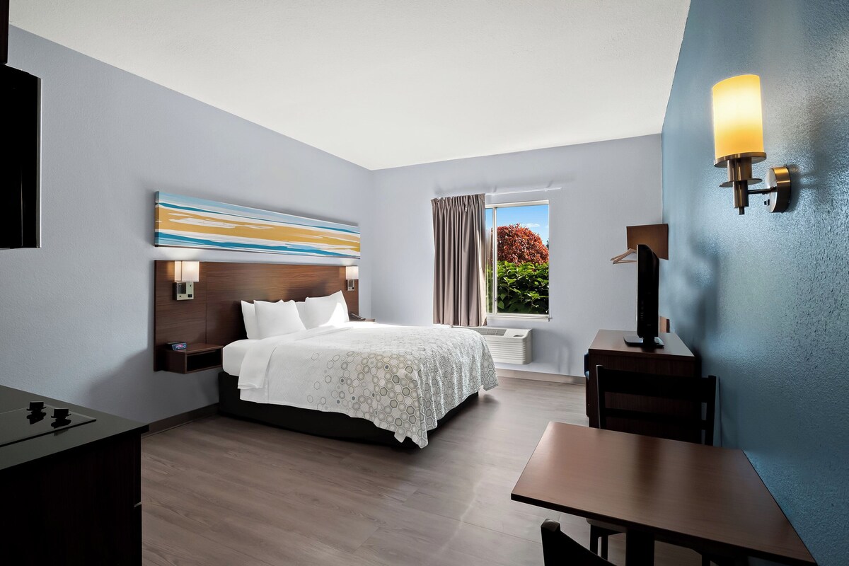 A modern hotel room with a bed, bedside table, desk, and a large window with curtains.
