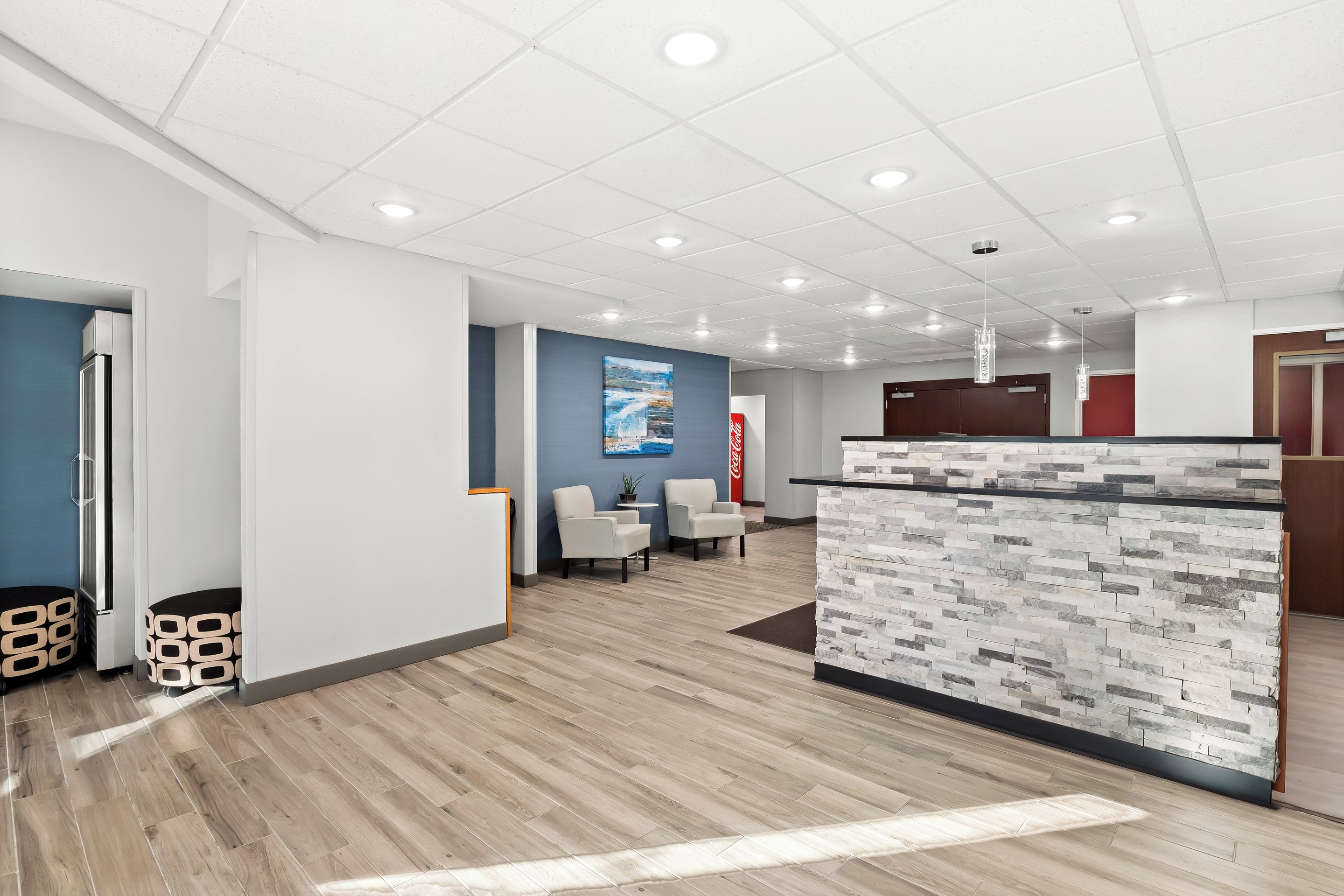 Un área de recepción moderna con mostrador de textura de piedra, pared de acento azul y una zona de estar con dos sillones.