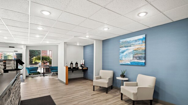 Eine moderne Lobby mit einer Rezeption, zwei Sitzbereichen mit Stühlen, einer Kaffeestation und einem großen Gemälde an der Wand.