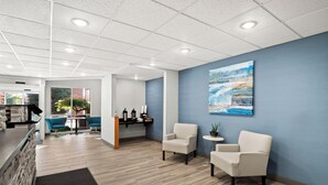 A modern lobby with a reception desk, two seating areas with chairs, a coffee station, and a large painting on the wall. - HomeTowne Studios by Red Roof East Lansing - Okemos (Okemos)