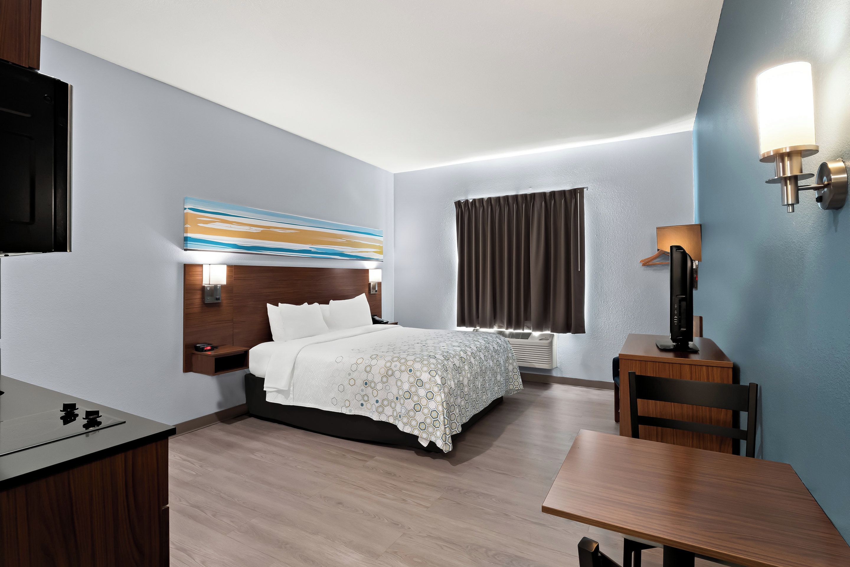 A modern hotel room with a bed, bedside table, desk, chair, and a TV.