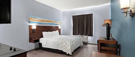 A modern hotel room with a bed, bedside table, desk, chair, and a TV.