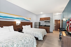 Una habitación de hotel con dos camas, kitchenette, televisor y un cuadro en la pared.