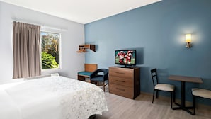A hotel room with a bed, a desk, a chair, a TV, and a window with curtains.