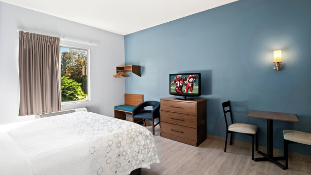 Une chambre d’hôtel avec un lit, un bureau, une chaise, une télévision et une fenêtre avec des rideaux.