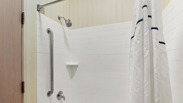 A bathroom with a white bathtub, a showerhead, and a grab bar.