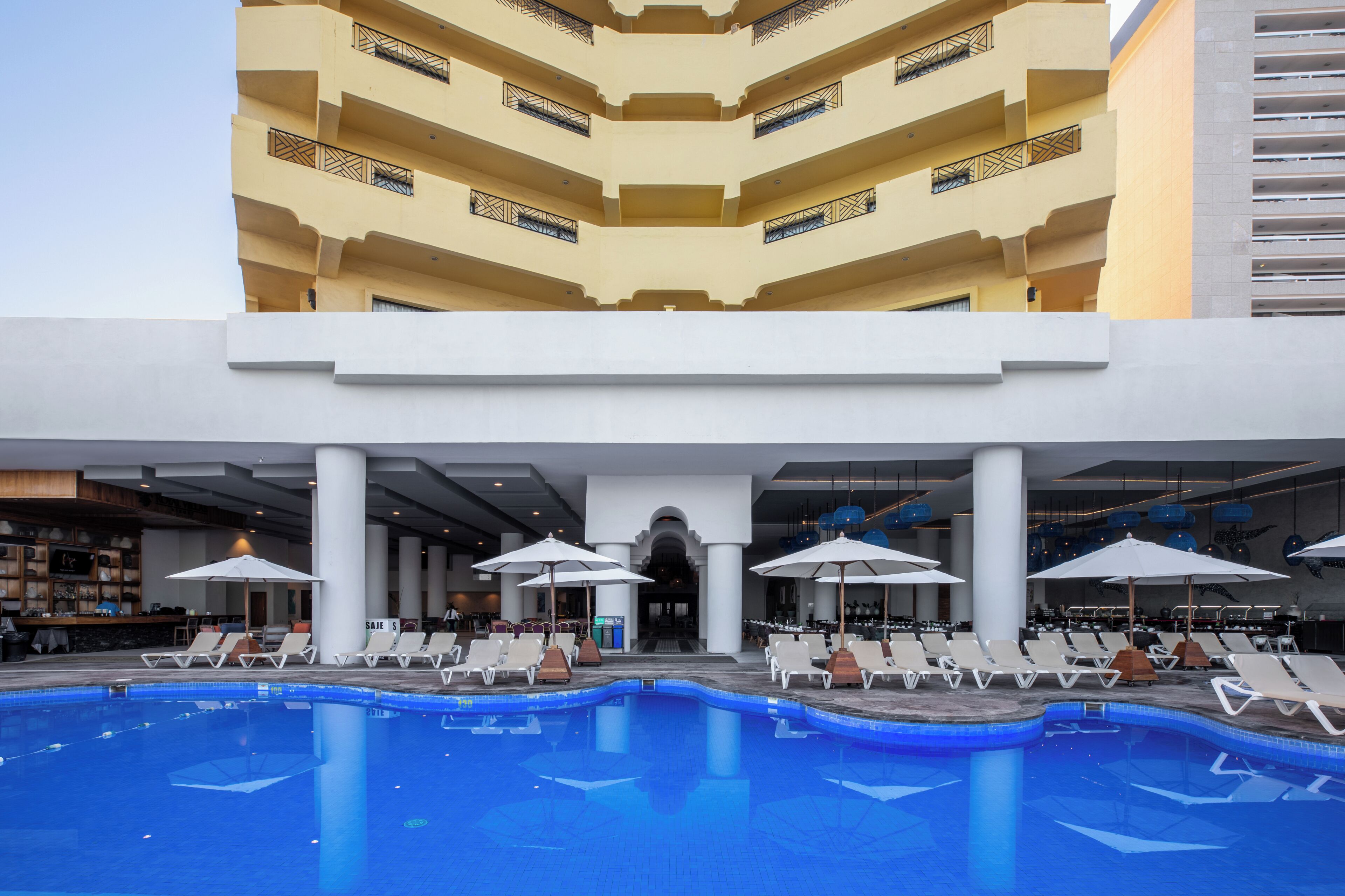 Un hotel con piscina, varias plantas y mobiliario exterior.