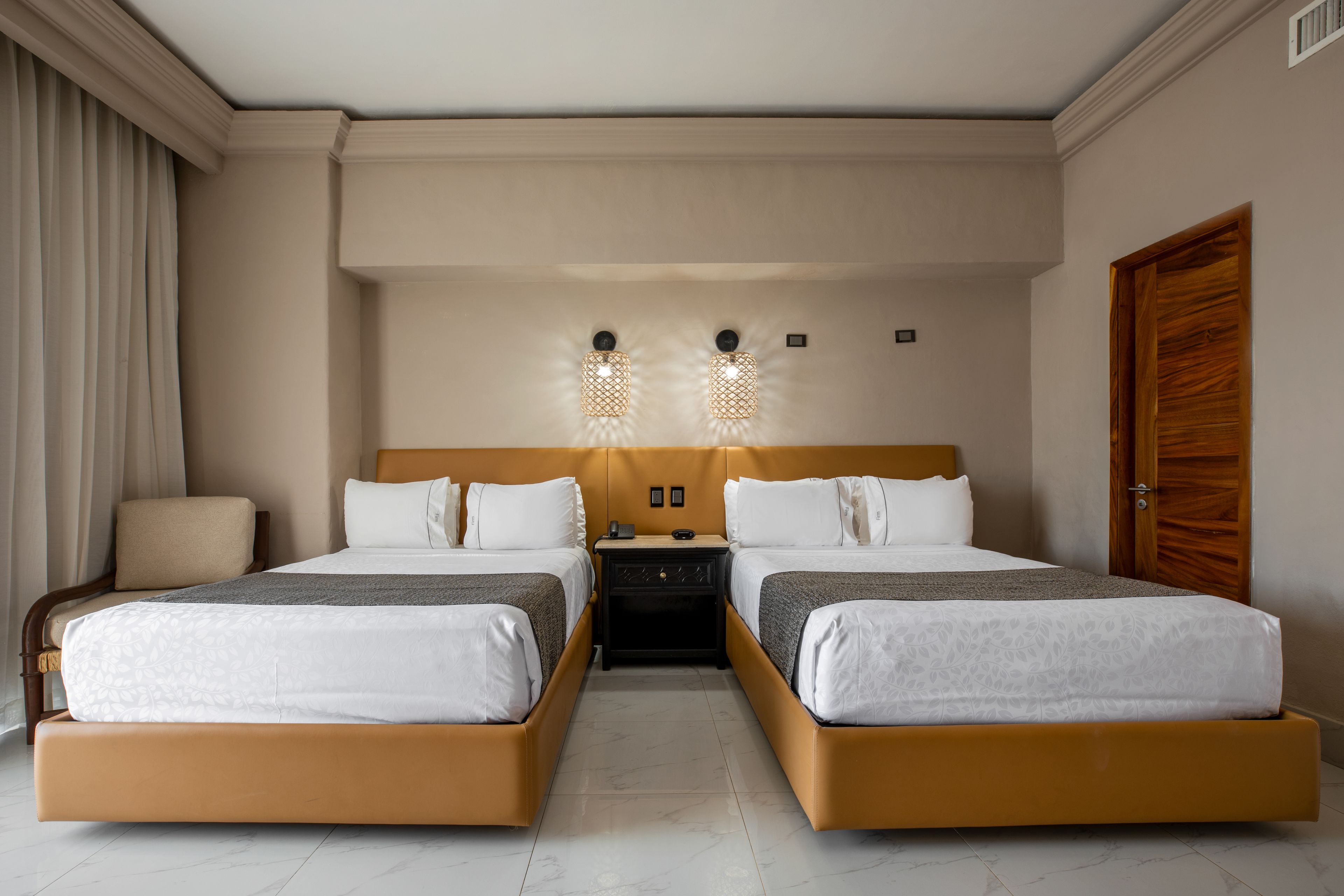 Ein Hotelzimmer mit zwei Betten, einem Nachttisch, einem Stuhl und einer Holztür.