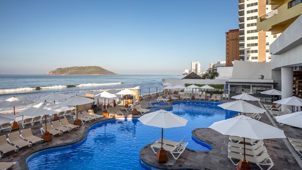 A pool area with lounge chairs and umbrellas, a view of the ocean, and a building labeled 'COSTA' in the background. - Royal Villas Resort (Mazatlán)