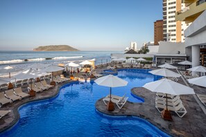 Ein Poolbereich mit Liegestühlen und Sonnenschirmen, mit Blick auf den Ozean, und ein Gebäude im Hintergrund mit der Aufschrift 'COSTA'.