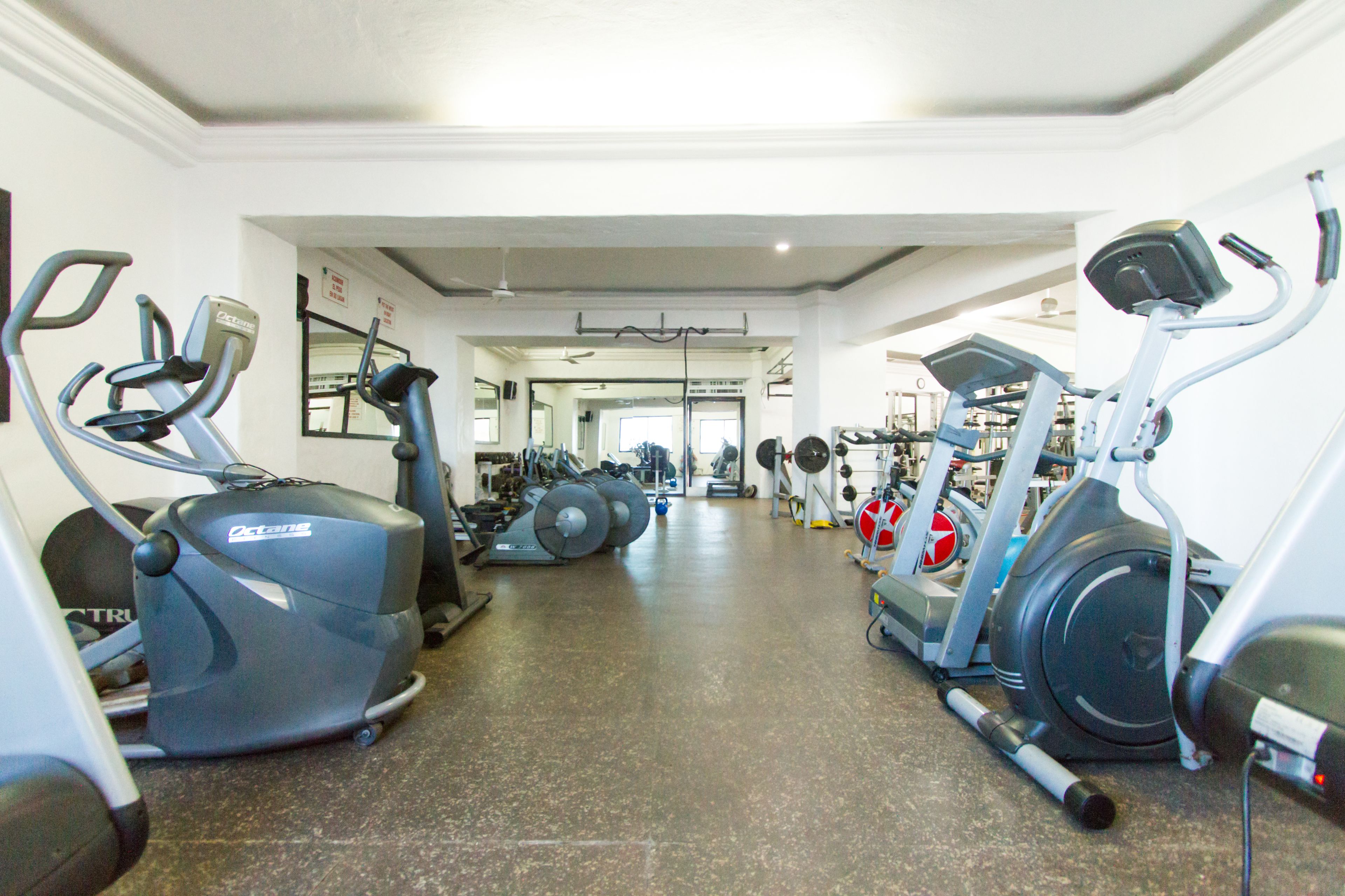 A gym with various cardio machines, weightlifting equipment, and a mirrored wall.