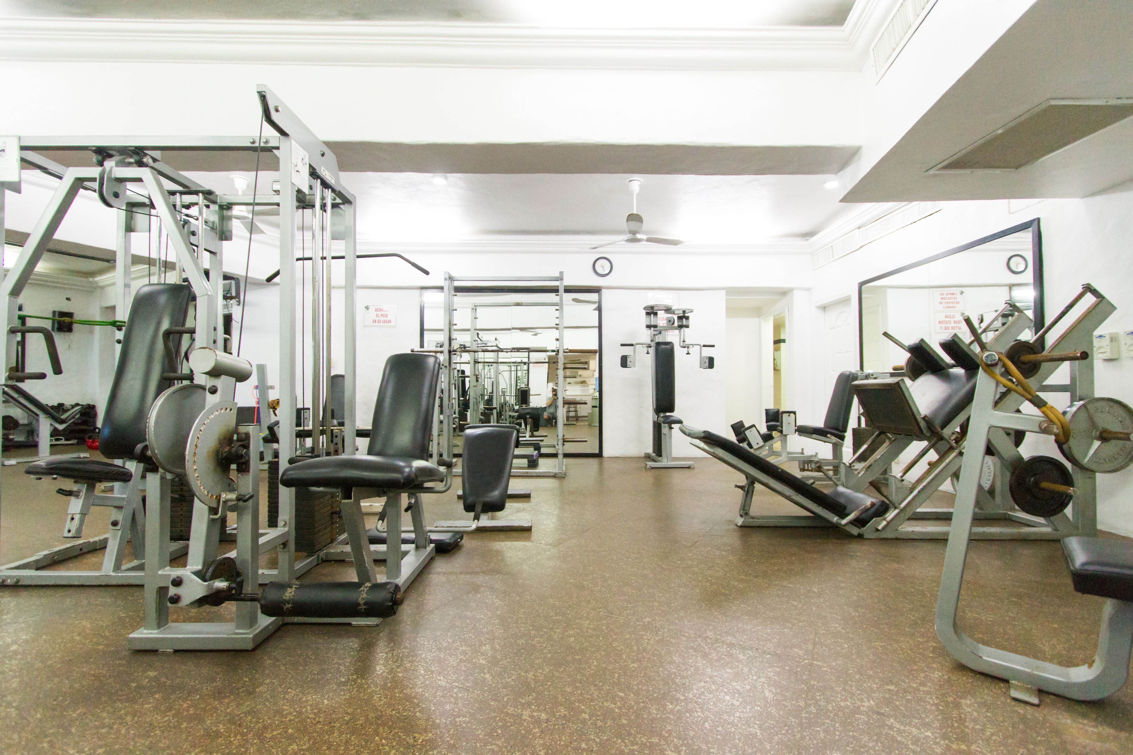 Een fitnessruimte met diverse fitnessapparaten, een plafondventilator en een deur naar een andere ruimte.