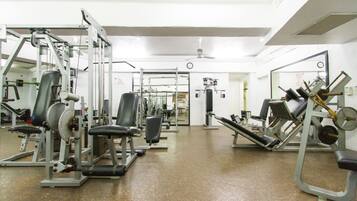 A gym with various exercise machines, a ceiling fan, and a door leading to another room.