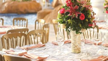 A table set for a formal event with a floral centerpiece, gold chairs, and white tablecloths.