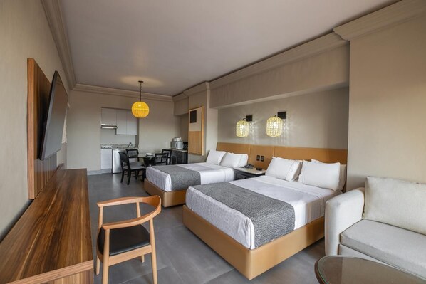 A hotel room with two beds, a desk, a chair, a sofa, and a TV.