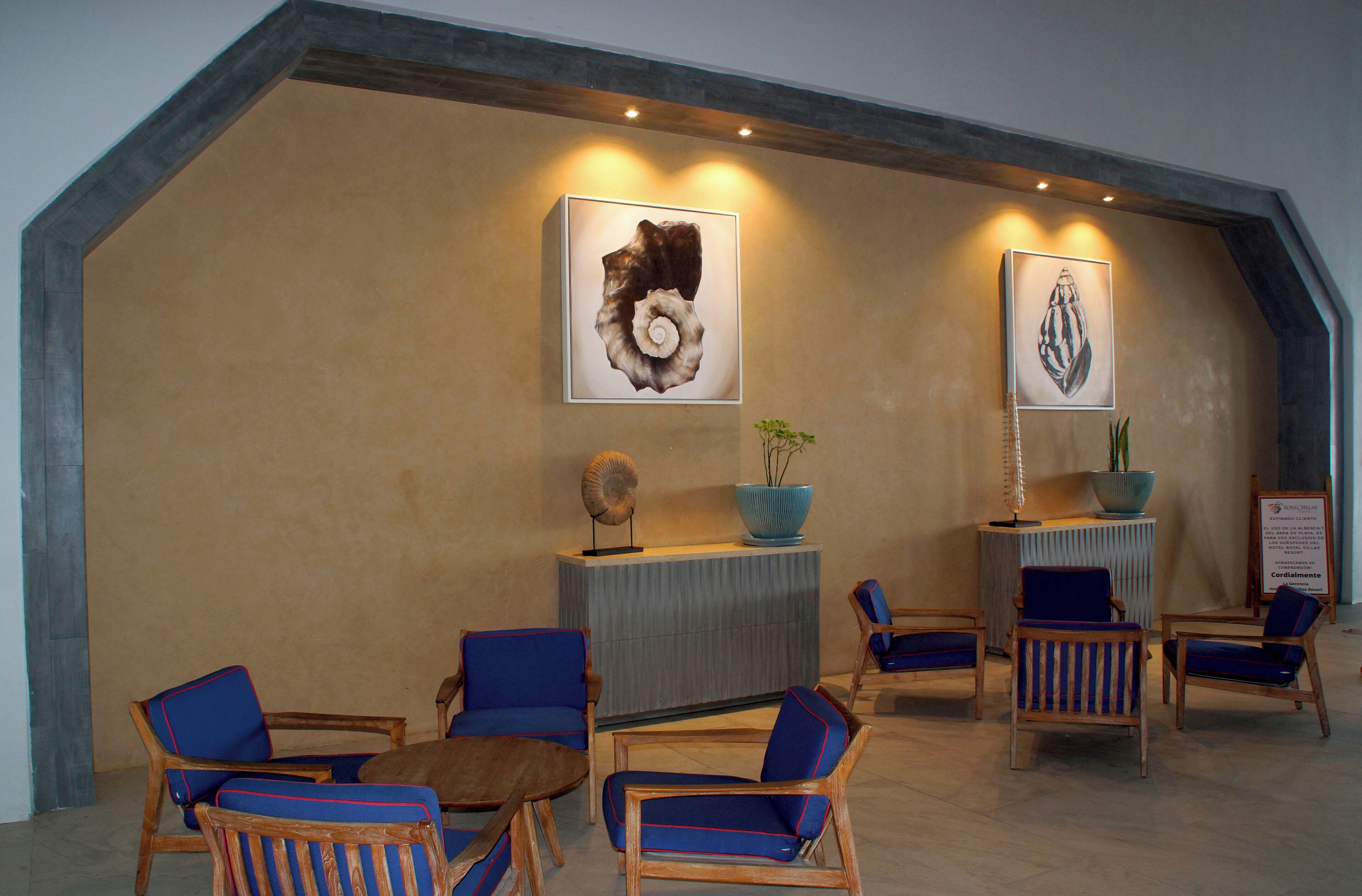 A lobby with wooden chairs and sofas, a reception desk, and two framed artworks on the wall.