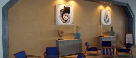 A lobby with wooden chairs and sofas, a reception desk, and two framed artworks on the wall.