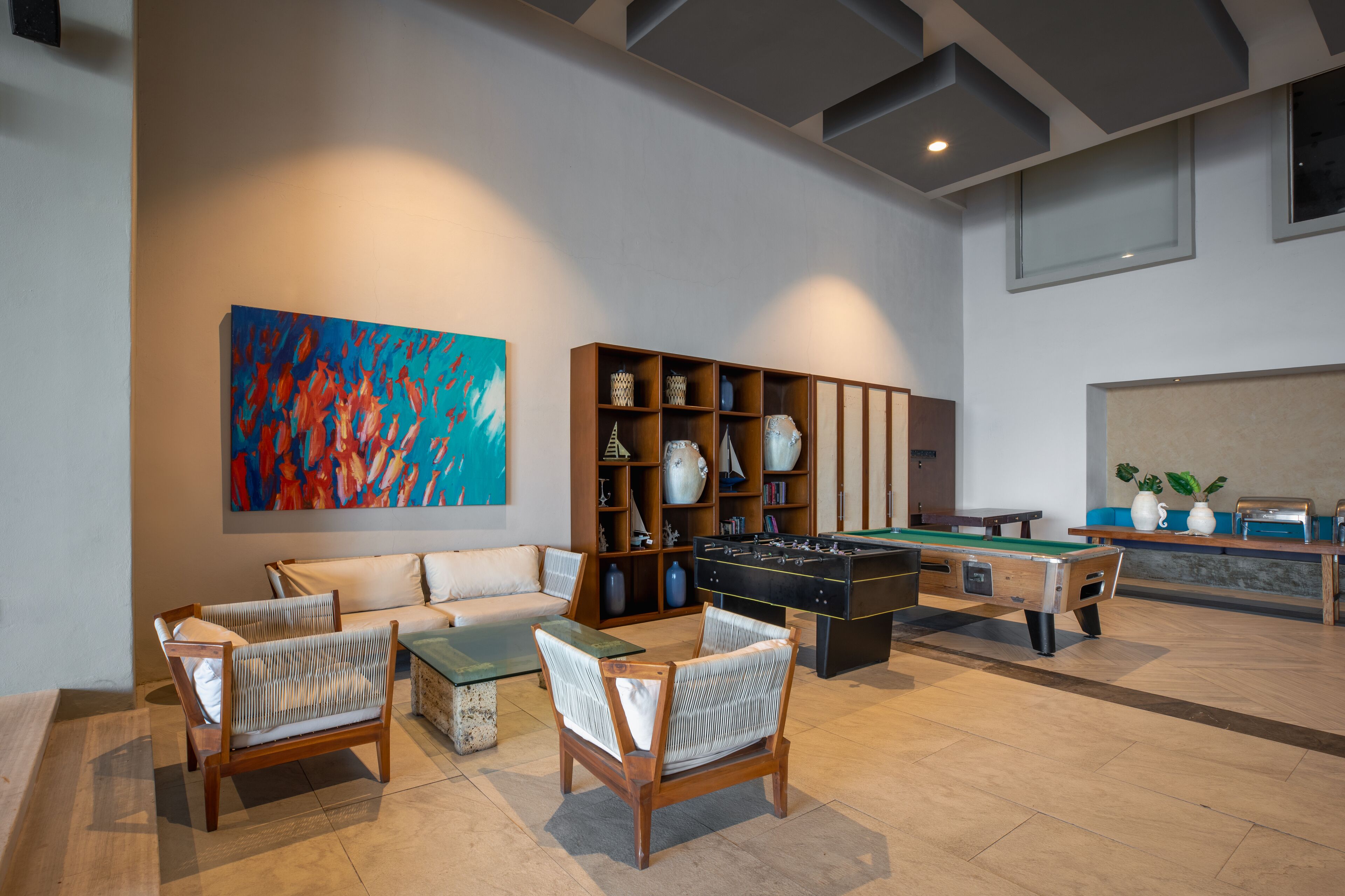 A modern lounge area with a pool table, comfortable seating, a bookshelf, and a vibrant abstract painting.