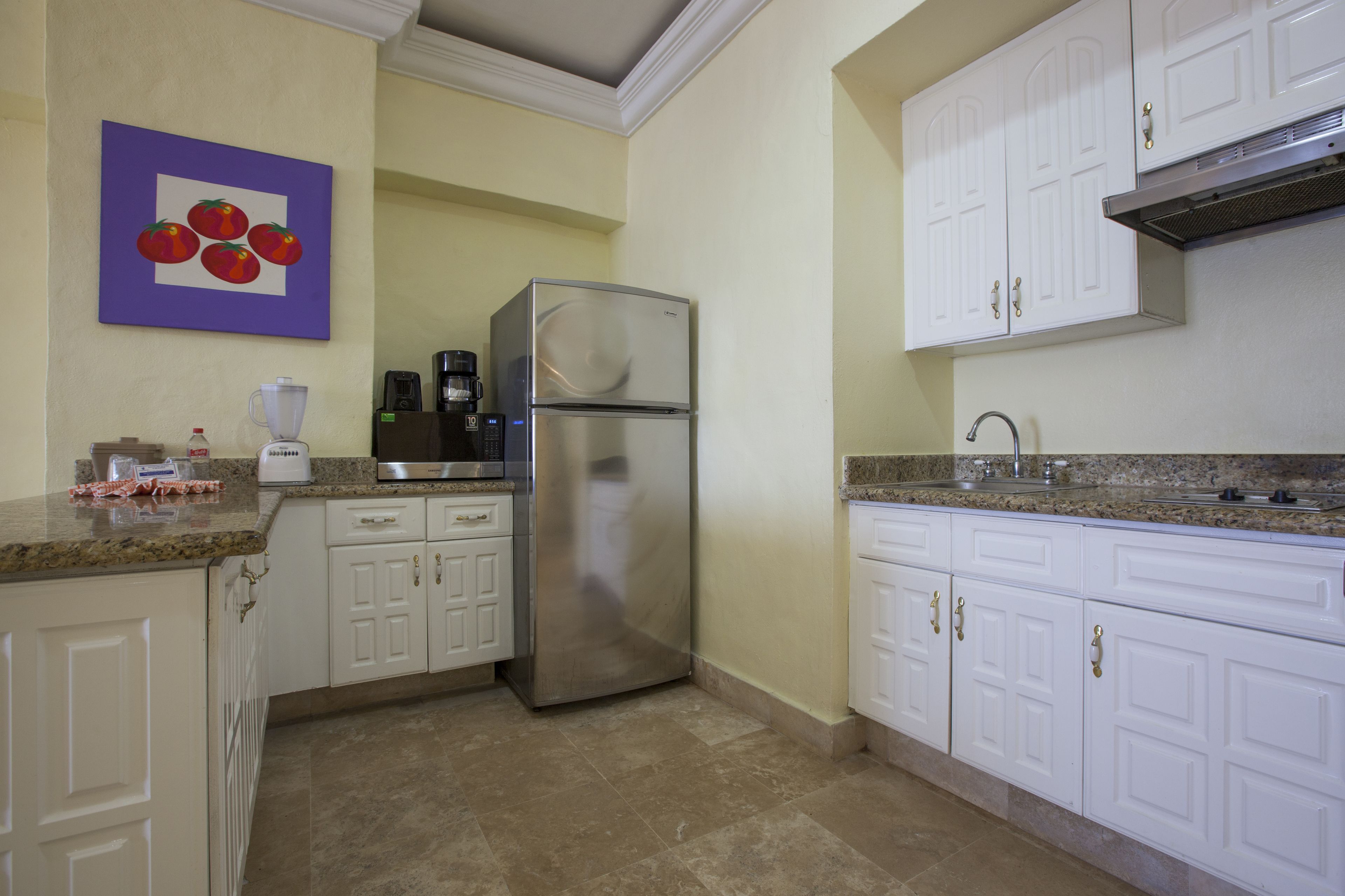 A kitchen with white cabinets, a stainless steel refrigerator, a granite countertop, and a coffee maker.