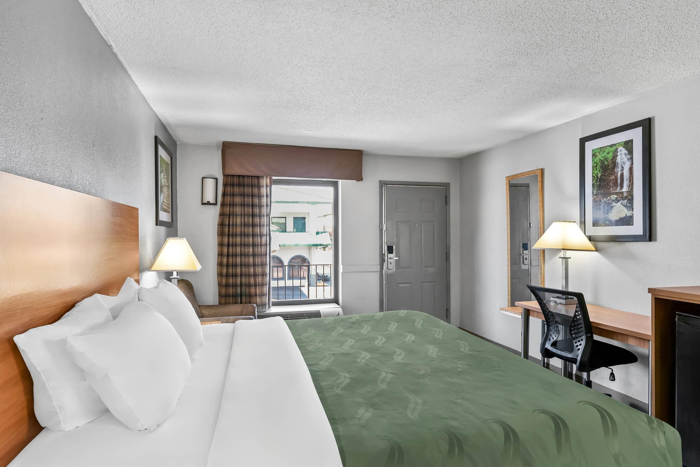 A hotel room with a bed, desk, chair, and a door leading to a balcony.