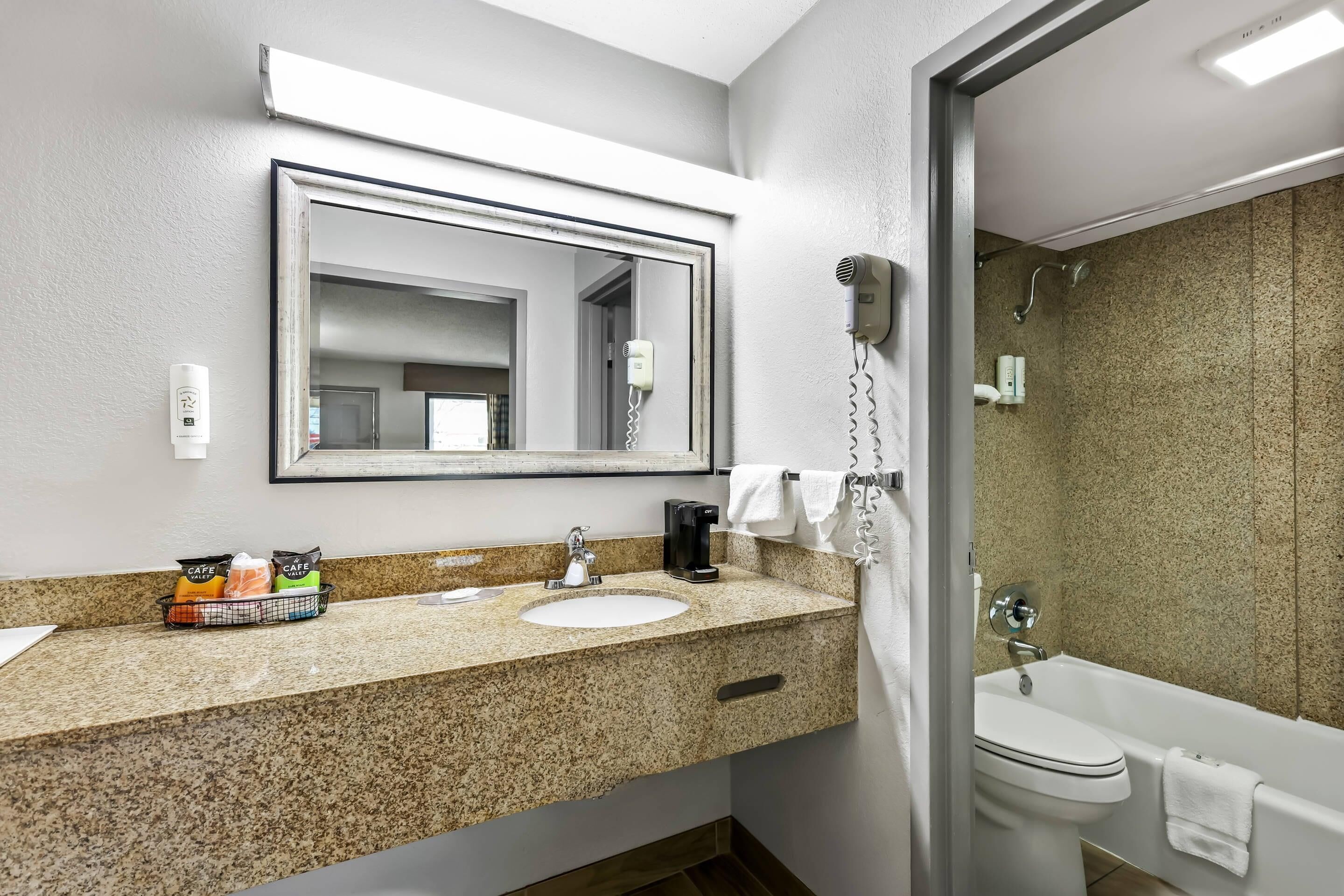 A bathroom with a granite countertop, a sink, a mirror, a hairdryer, a shower, and a toilet.