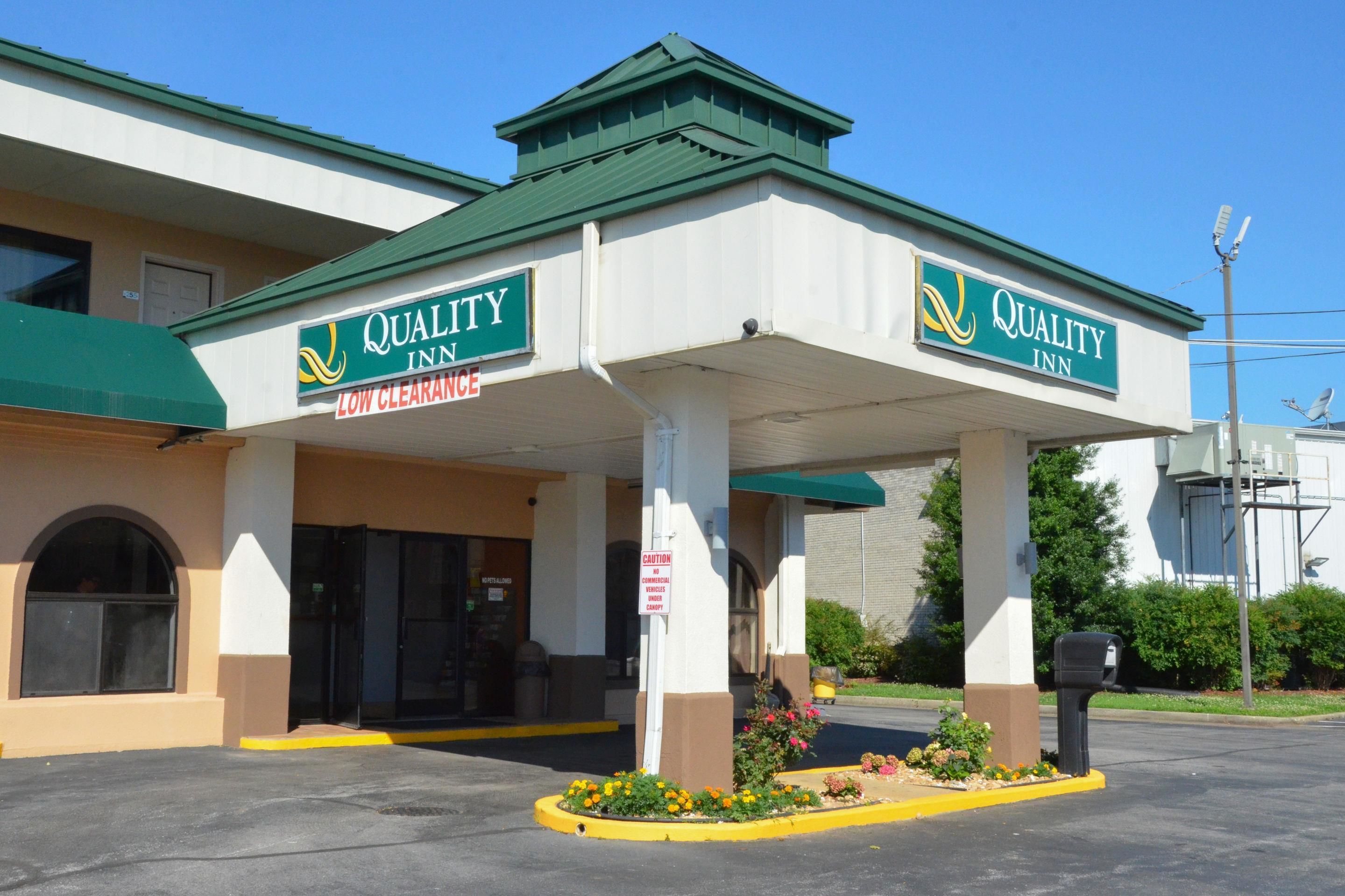 A Quality Inn with a green roof, a sign indicating low clearance, and a parking lot with a yellow curb.