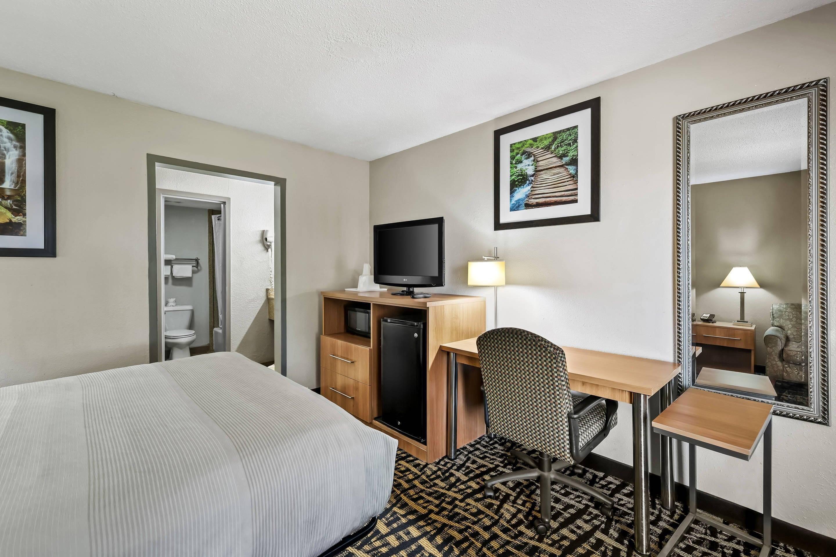 A hotel room with a bed, desk, chair, television, and a mirror.