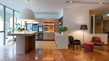 A modern lobby with a reception desk, vending machines, seating area, and a large window.