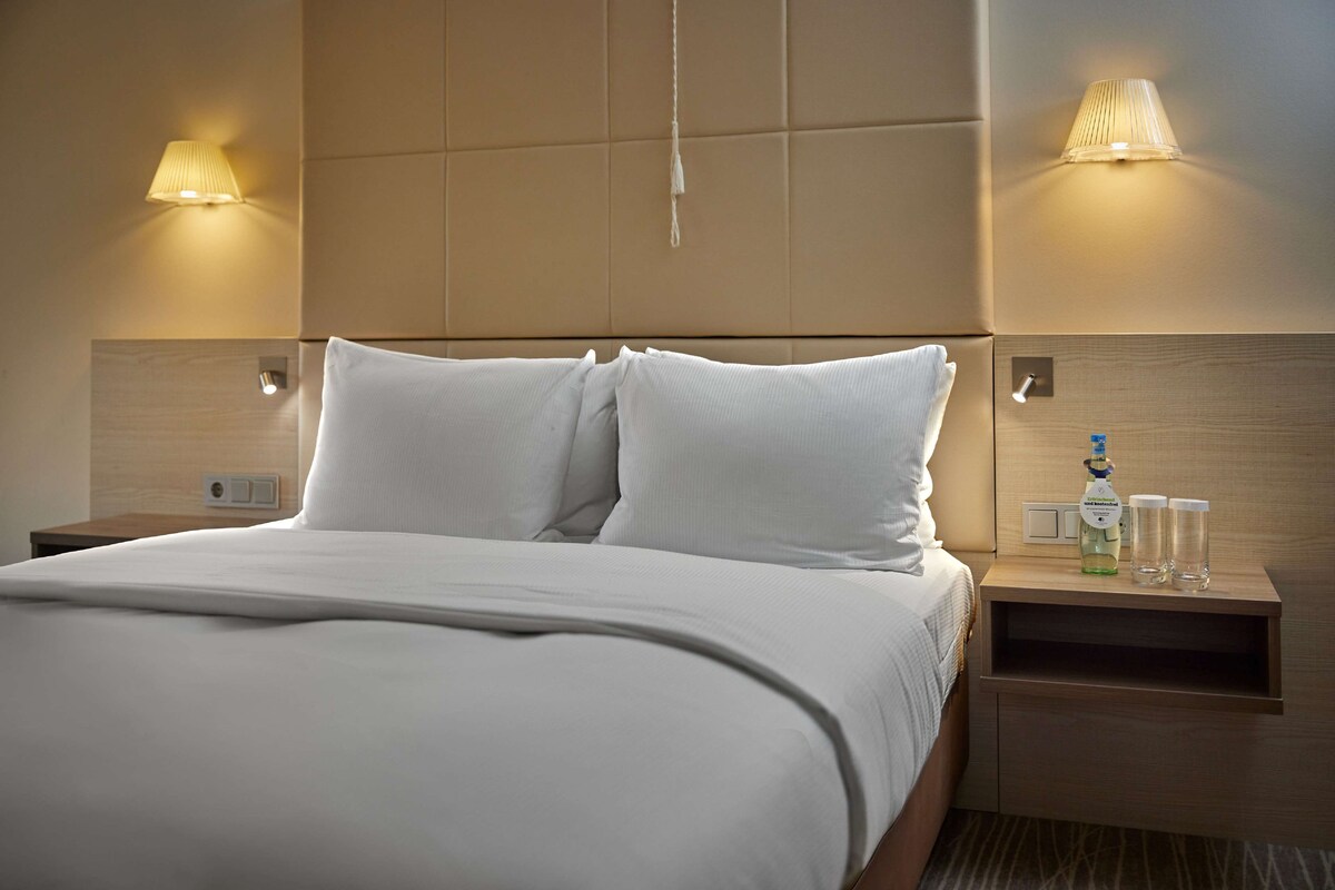 A neatly made bed with white linens, a wooden headboard, and two bedside lamps.