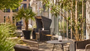 An outdoor patio area with wicker furniture, a palm tree, and a sign for The Soulbird SPA Albertz. - DoubleTree by Hilton Hannover Schweizerhof (Hannover)