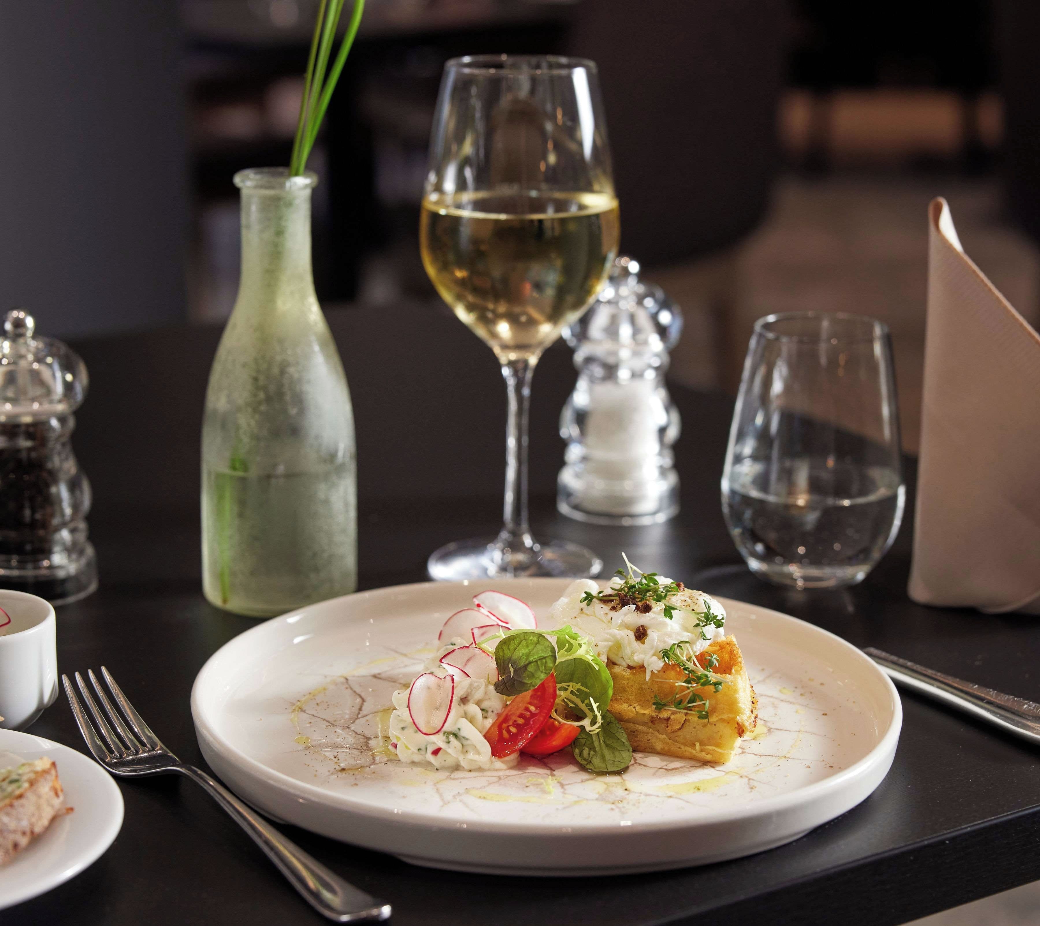 A dining table with a plate of food, a glass of white wine, and a salt and pepper shaker.