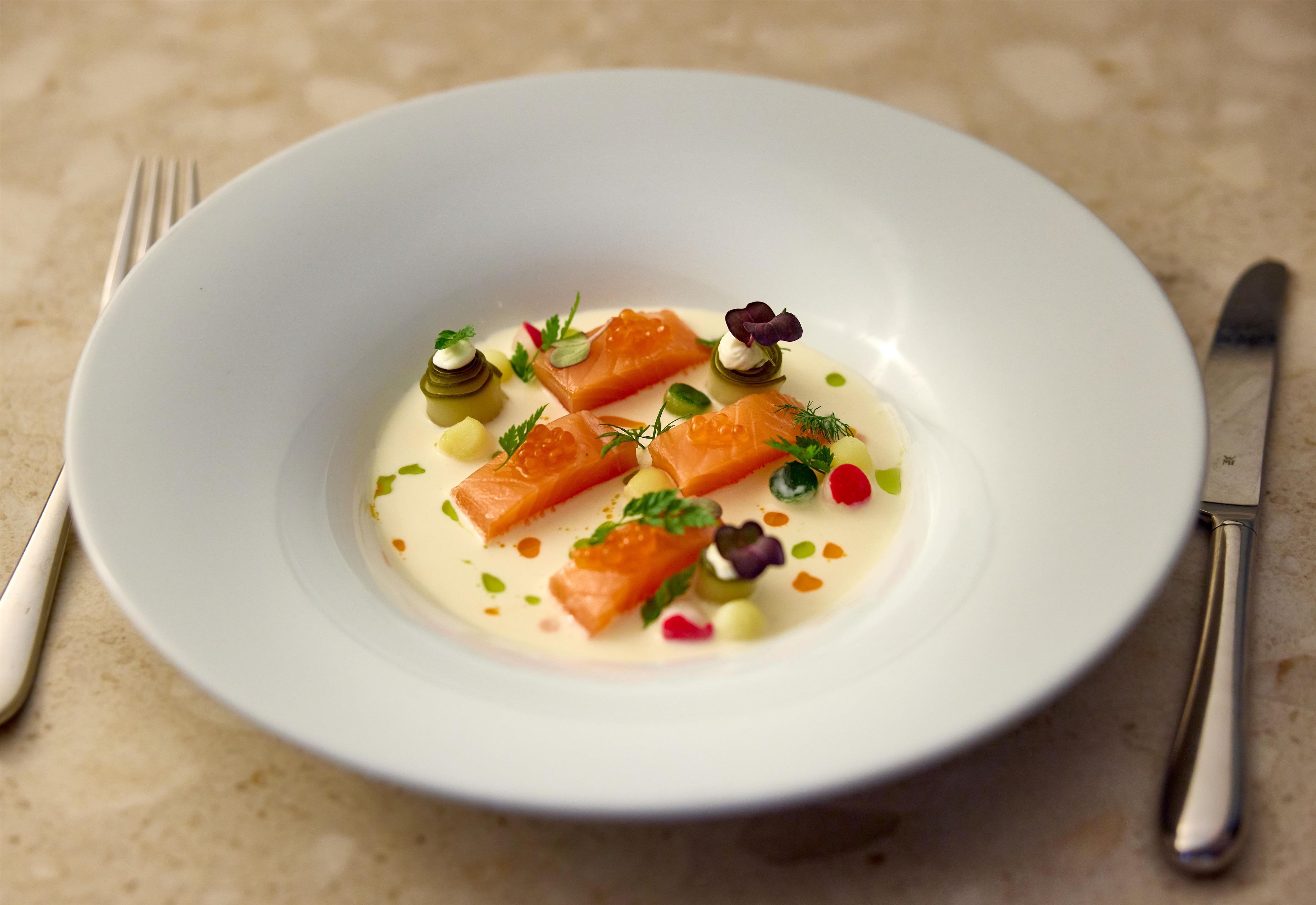 A white plate with salmon, cream, and garnishes on a textured surface.