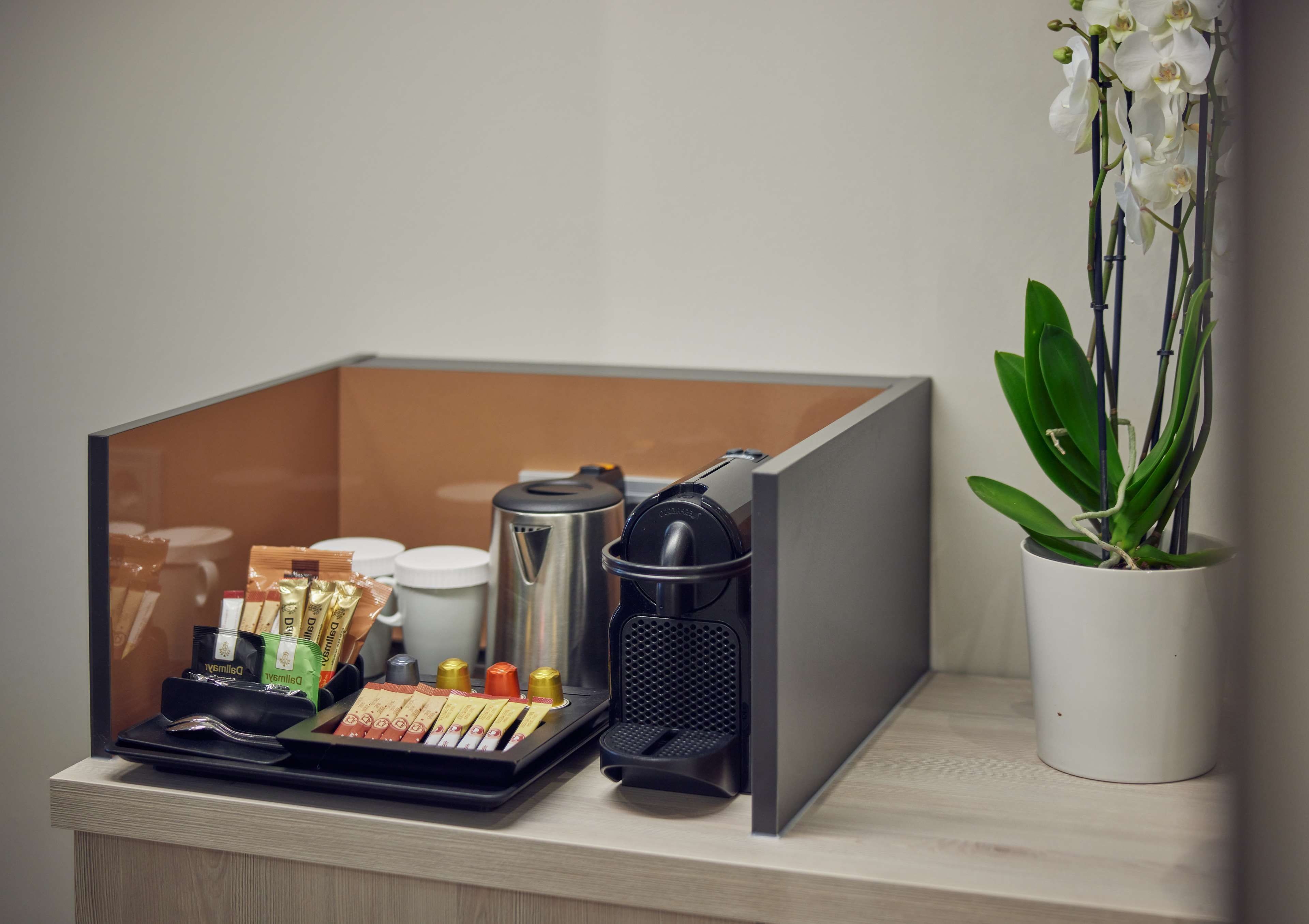 A compact kitchenette with a coffee maker, tea packets, a kettle, and a potted orchid.