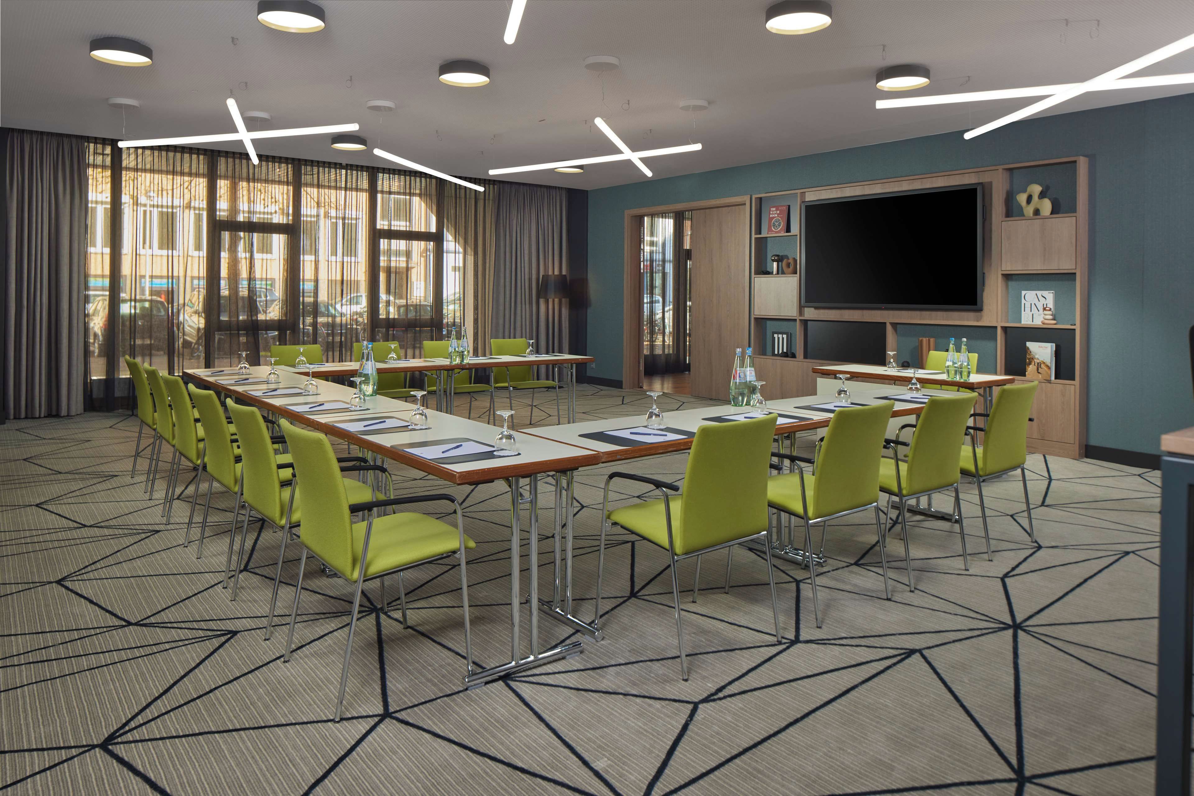 A conference room with a large table, multiple chairs, a flat-screen TV, and a bookshelf.