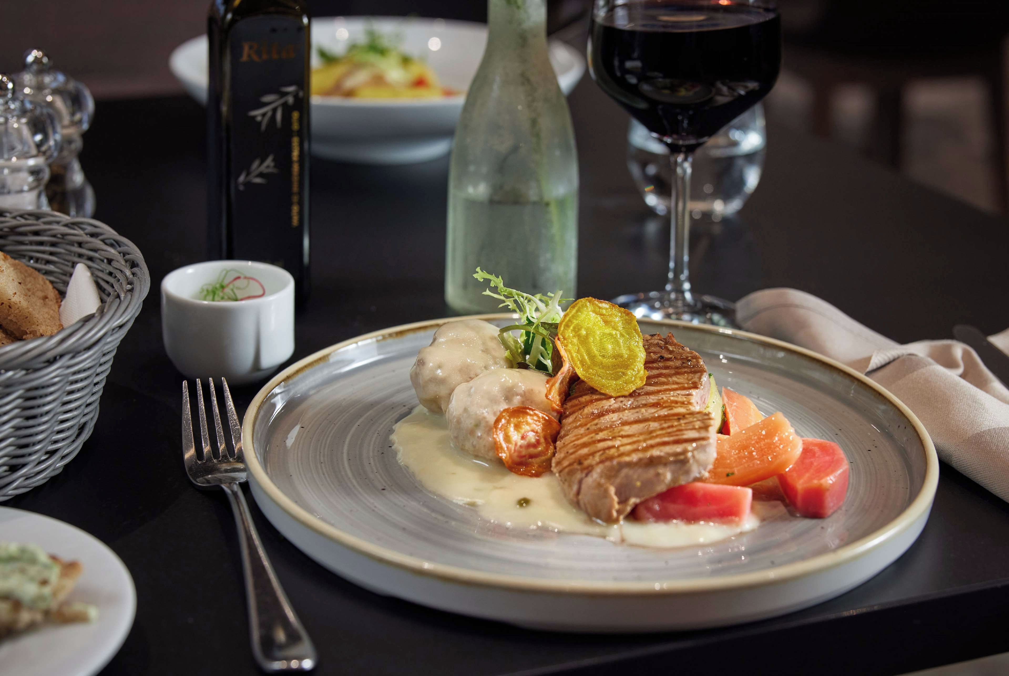 Un plato de comida con una botella y una copa de vino tinto sobre la mesa.