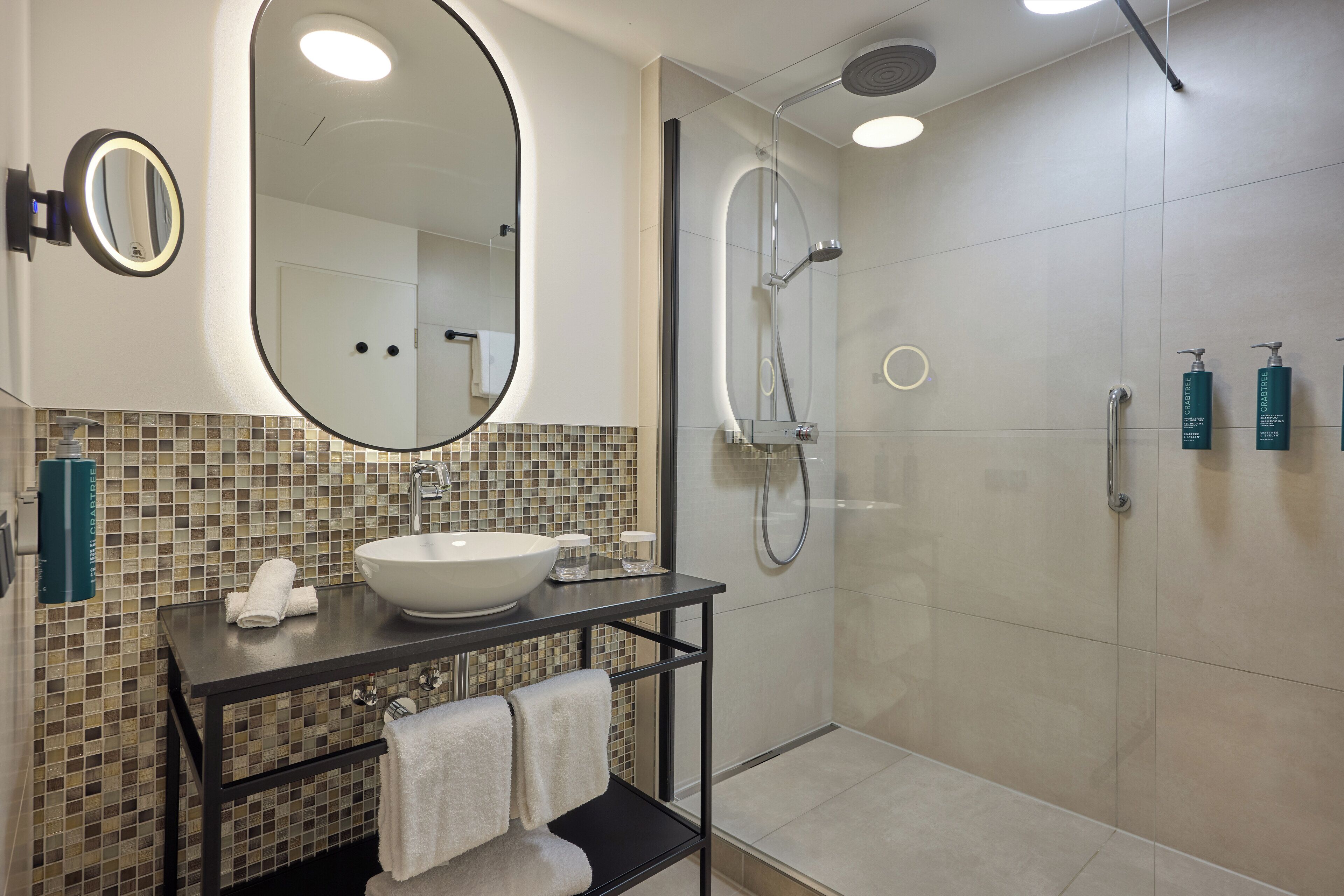 Een moderne badkamer met een grote spiegel, een wastafel, een douche en toiletartikelen aan de muur.