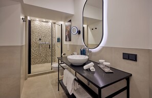 Un baño moderno con un espejo grande, un lavabo blanco y una ducha con mampara de vidrio.