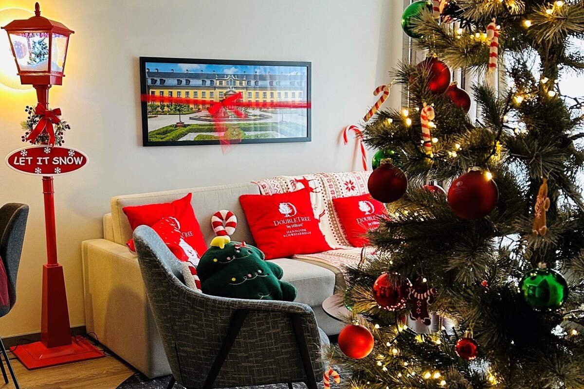 A cozy living room with a Christmas tree, a red street lamp, and a framed picture of a building.