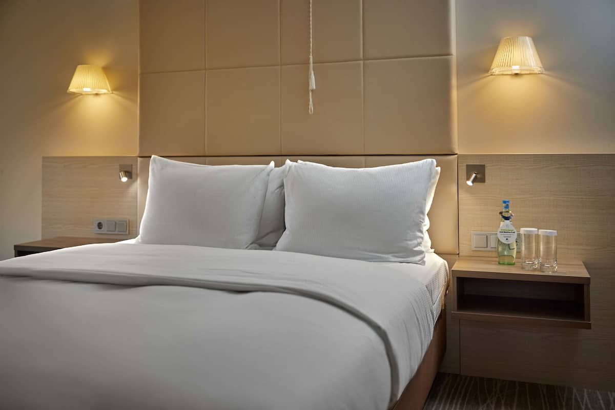 A neatly made bed with white linens, a wooden headboard, and two bedside lamps.