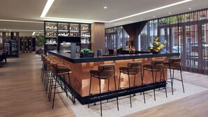 A modern bar area with a long counter, multiple stools, and a variety of bottles on shelves. - DoubleTree by Hilton Hannover Schweizerhof (Hannover)