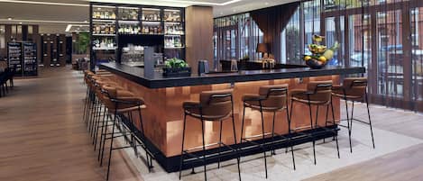 Un bar moderno con una barra larga, varios taburetes y una variedad de botellas en estantes.